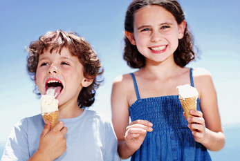 Un niño y su hermana disfrutando de su helado afuera.